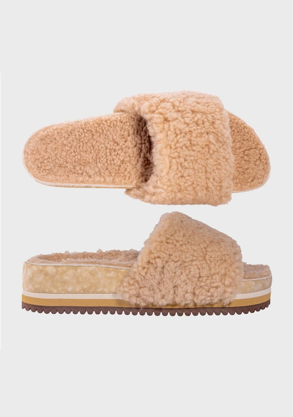 [Color: Sand] An image of a fuzzy shearling slide sandal in beige with a thick platform sole. Designed with sustainability in mind from Fleks footwear. 