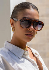 [Color: Blue Tortoise] A woman wearing sunglasses with a tortoise frame and blue lenses from FREYRS.