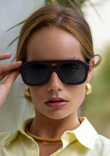 [Color: Burgundy] Woman wearing sunglasses with a burgundy frame from FREYRS.