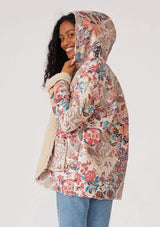 [Color: Natural/Red] A front facing image of a brunette model wearing a bohemian jacket with a pink and natural floral print and a faux shearling lining. With long sleeves, side pockets, a hoodie, and an open front.