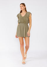 [Color: Olive] A full body front facing image of a brunette model wearing an olive green bohemian short romper. With short flutter sleeves, a v neckline, a crochet top, a self covered button front top, and a smocked elastic waist. 