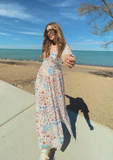 [Color: Ivory/Orange] A front facing image of a blonde model near the beach wearing a blue and orange kimono sleeve maxi dress with a deep v neckline, smocked waist, tie back detail, and side slits. 