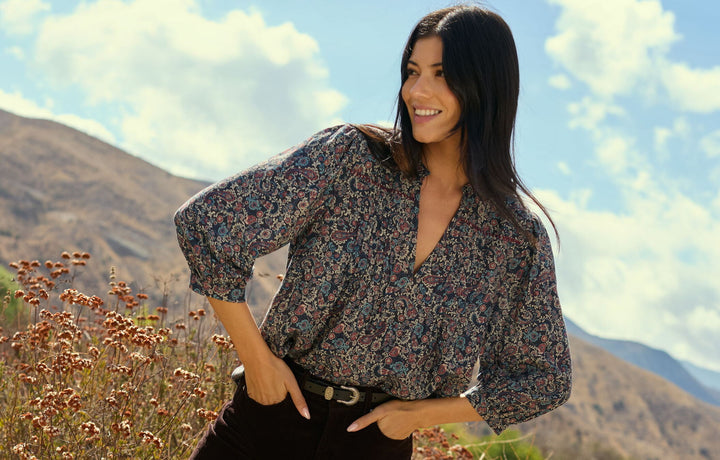 Woman in a floral blouse standing outdoors with mountains in the background