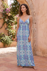 [Color: Blue/Mint] A front facing image of a brunette model in a courtyard with greenery wearing a blue bohemian printed maxi dress with spaghetti straps, a v neckline, and an empire waist. 