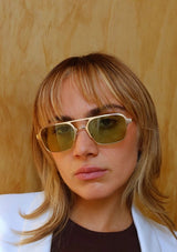 [Color: Green] A woman wearing a matte gold metal straight frame sunglasses with 100% UVA/UVB protected green lenses. 