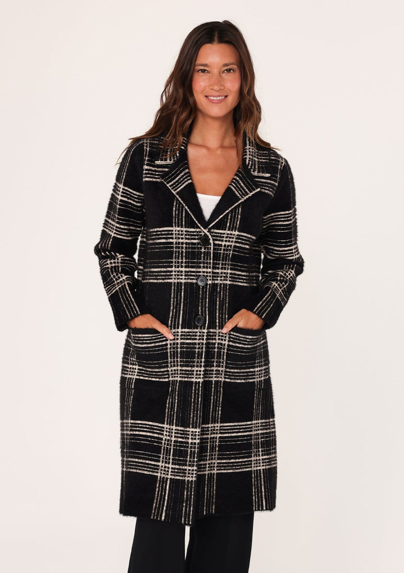 [Color: Black/Cream] A front facing image of a brunette model wearing a cozy and fuzzy sweater coat in a black and cream plaid pattern. With long sleeves, a notched lapel, side patch pockets, and a button front. 