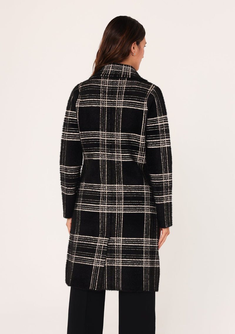 [Color: Black/Cream] A back facing image of a brunette model wearing a cozy and fuzzy sweater coat in a black and cream plaid pattern. With long sleeves, a notched lapel, side patch pockets, and a button front. 