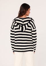 [Color: Black/White] A back facing image of a brunette model wearing a black and white striped knit hoodie. With long sleeves, a dropped shoulder, a v neckline, and a front kangaroo pocket. 