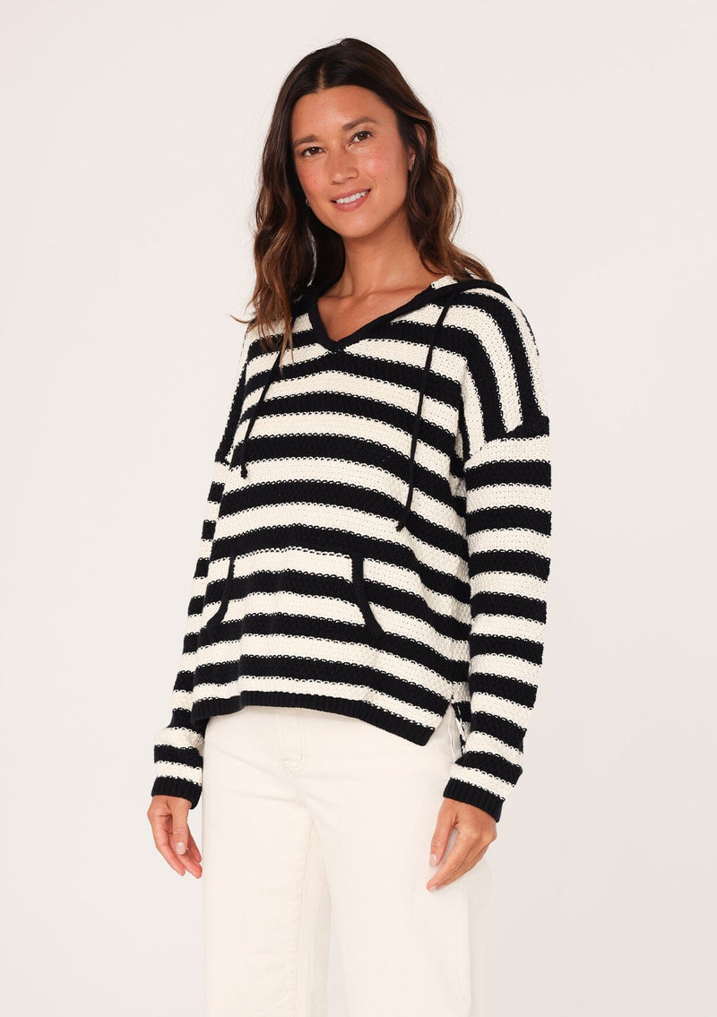 [Color: Black/White] A half body side facing image of a brunette model wearing a black and white striped knit hoodie. With long sleeves, a dropped shoulder, a v neckline, and a front kangaroo pocket. 
