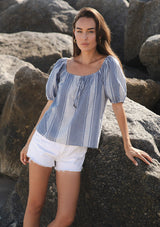 [Color: Navy/White] A front facing image of a brunette model by rocks wearing a blue and white checkered puff sleeve top with an elastic round neckline. 