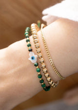 [Title: Malachite]  An adjustable healing bracelet, crafted on a durable nylon cord with a mother of pearl hamsa stone, gold-plated hardware and green natural gemstones. Designed by Kindred Row.