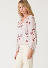 [Color: Dusty Blush/Wine] A side facing image of a blonde model wearing a bohemian resort blouse crafted from textured chiffon and designed in a pink floral print. With a decorative button front, a v neckline, long raglan sleeves, and an elastic waist. 