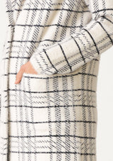[Color: Cream/Black] A close up side facing image of a blonde model wearing a fuzzy statement sweater coat in a cream and black plaid print. With long sleeves, a notched collar, a snap button front, and side patch pockets. 