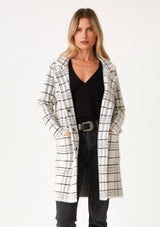 [Color: Cream/Black] A front facing image of a blonde model wearing a fuzzy statement sweater coat in a cream and black plaid print. With long sleeves, a notched collar, a snap button front, and side patch pockets. 