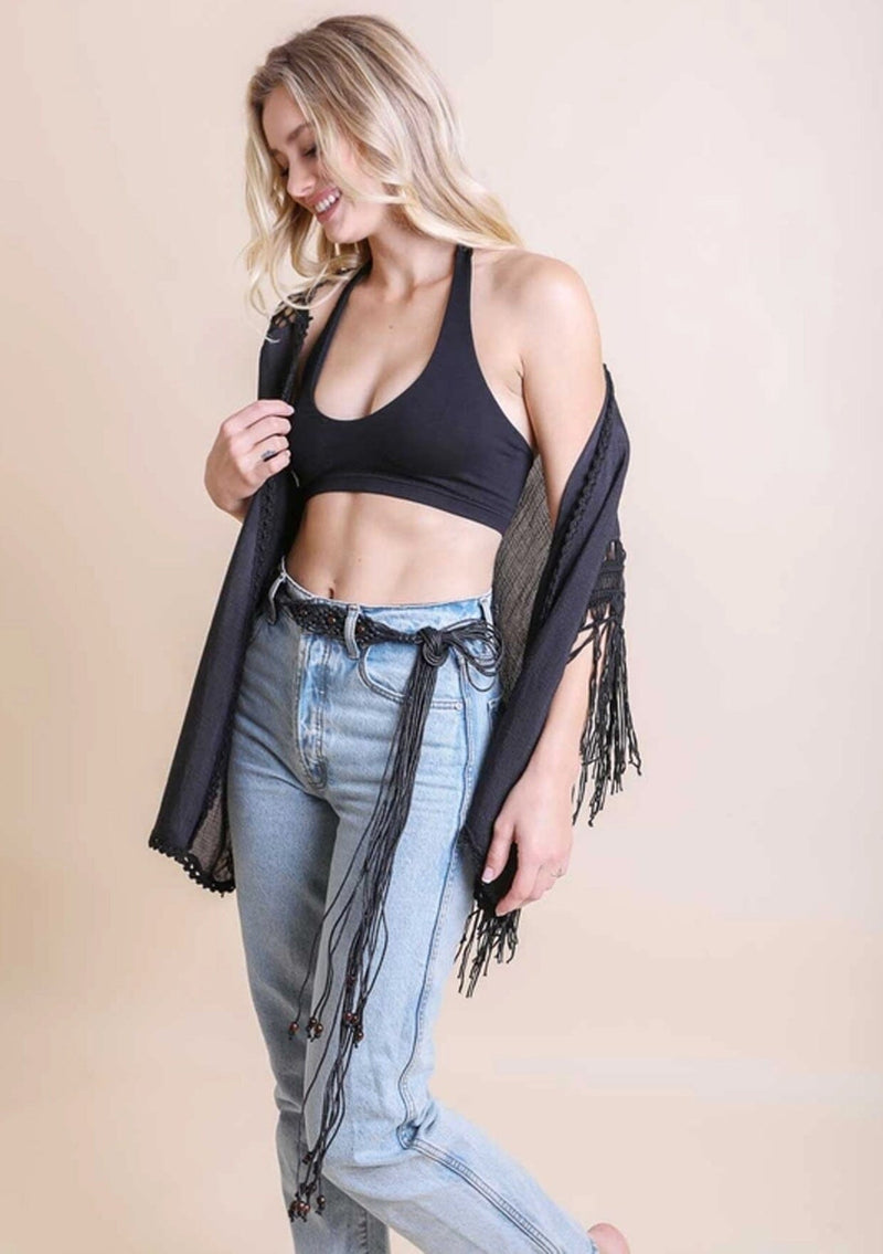 [Color: Black] A blonde model wearing a a long bohemian macrame belt with beads wrapped around denim bottoms.