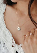 [Color: Gold] A woman wearing a gold chain necklace with a gold disc with mama on it. 