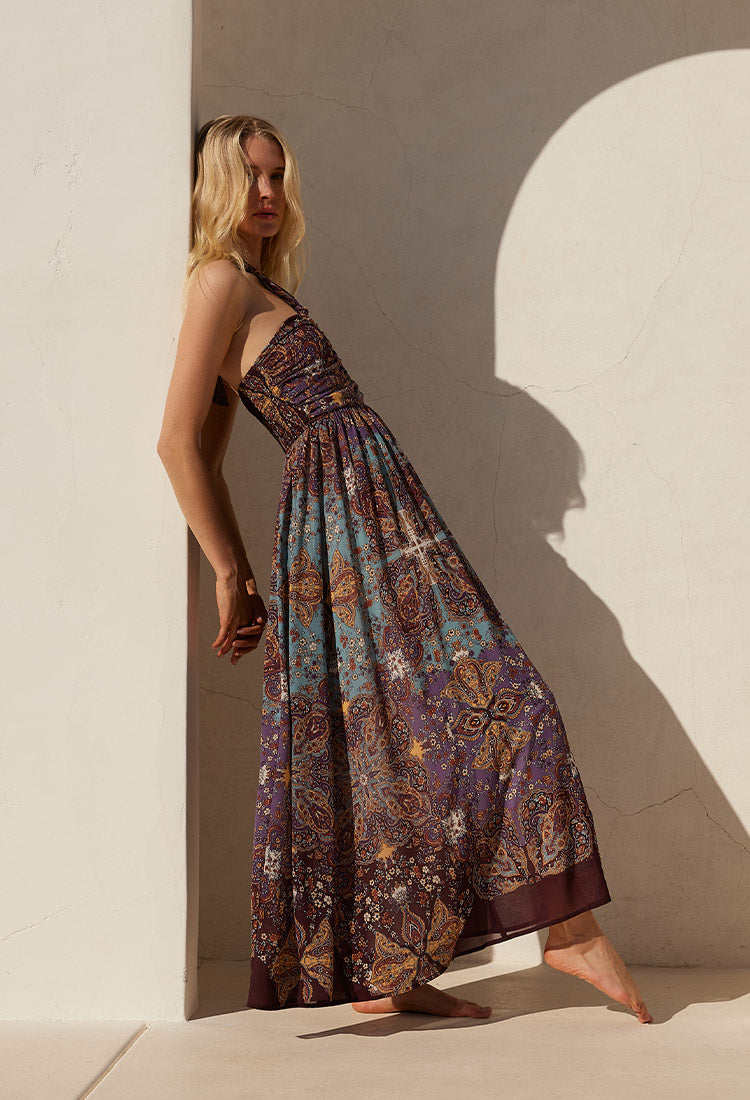 Lovestitch purple bohemian floral print halter maxi dress in a chic Moroccan print. Model is standing in front of a Spanish style resort doorway. The perfect vacation dress!