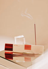 Incense sticks with a box on a reflective surface against a beige background