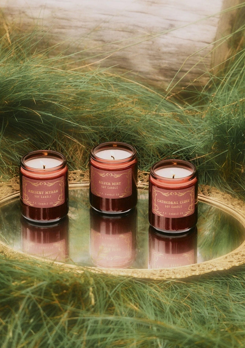 A fall and holiday candle in a burgundy glass jar labeled “P.F. Candle Co. Cathedral Clove.”