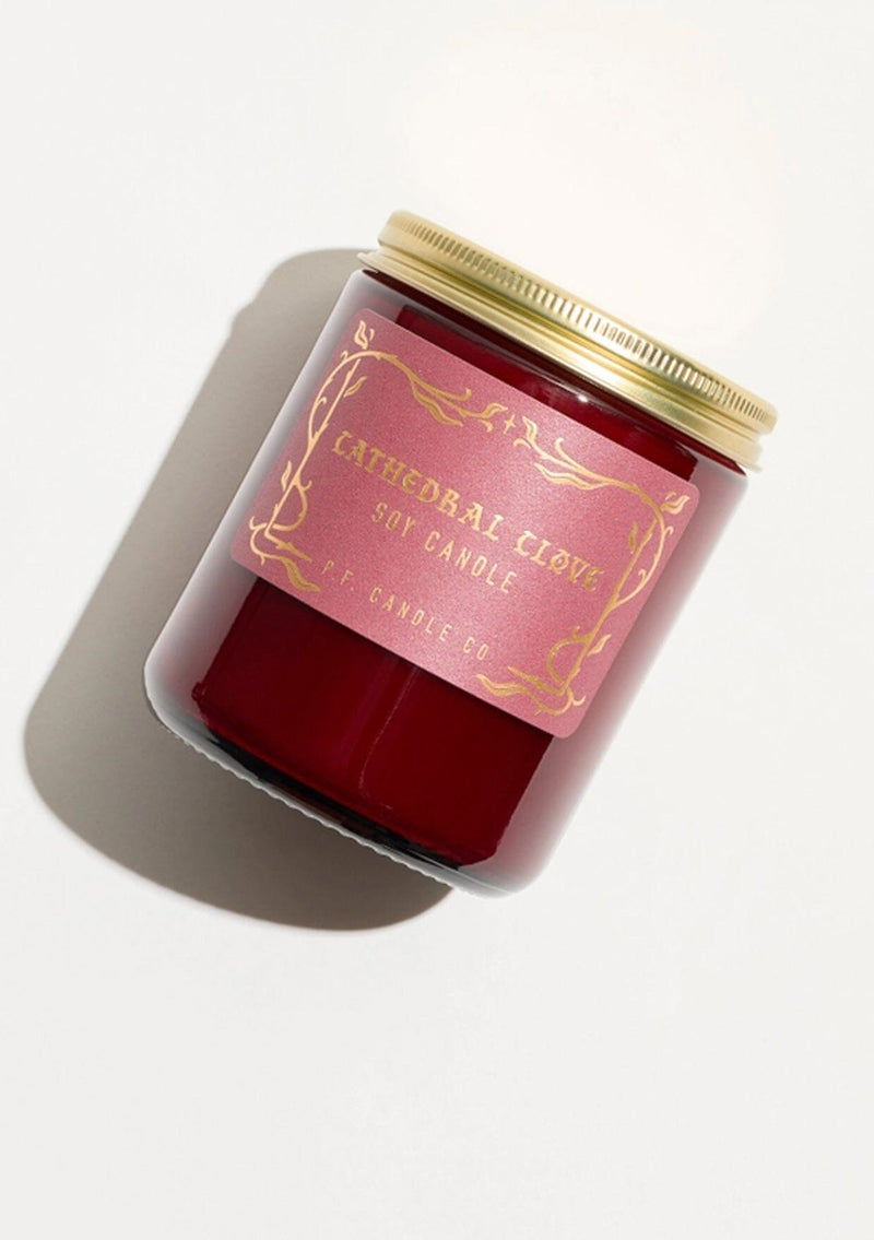A fall and holiday candle in a burgundy glass jar labeled “P.F. Candle Co. Cathedral Clove.”