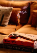 Incense stick burning on a book with a blurred sofa in the background