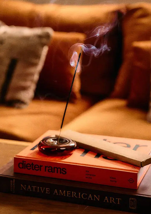 Incense stick burning on a book with a blurred sofa in the background