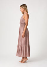 [Color: Rose Water] A side facing image of a blonde model wearing a pink bohemian maxi dress in a soft pink vintage wash. With a ruffle trimmed halter neckline, a smocked elastic waist, a tiered long skirt, and a back keyhole detail with an adjustable tie. 