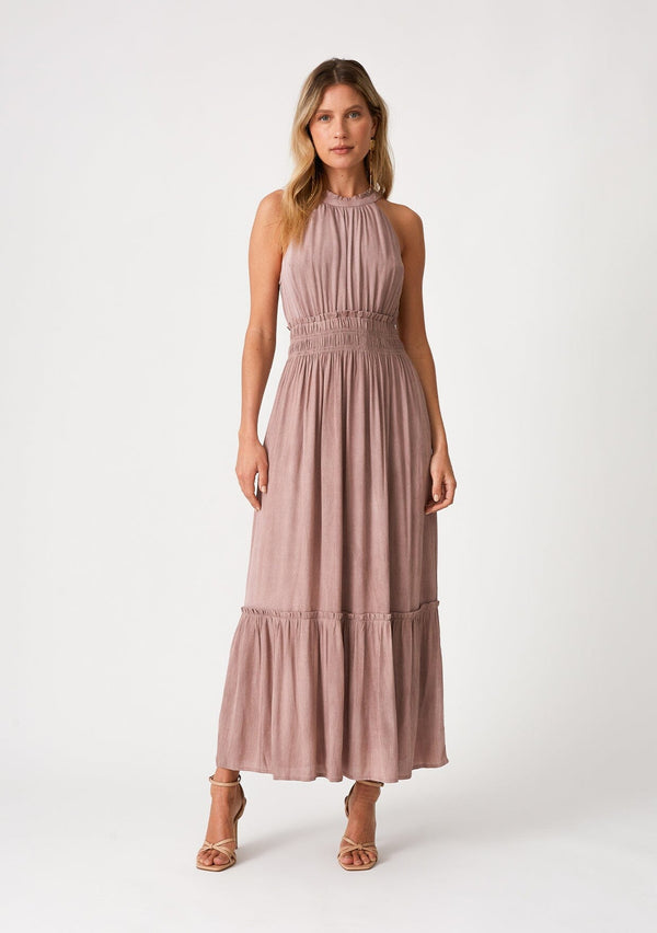 [Color: Rose Water] A front facing image of a blonde model wearing a pink bohemian maxi dress in a soft pink vintage wash. With a ruffle trimmed halter neckline, a smocked elastic waist, a tiered long skirt, and a back keyhole detail with an adjustable tie. 