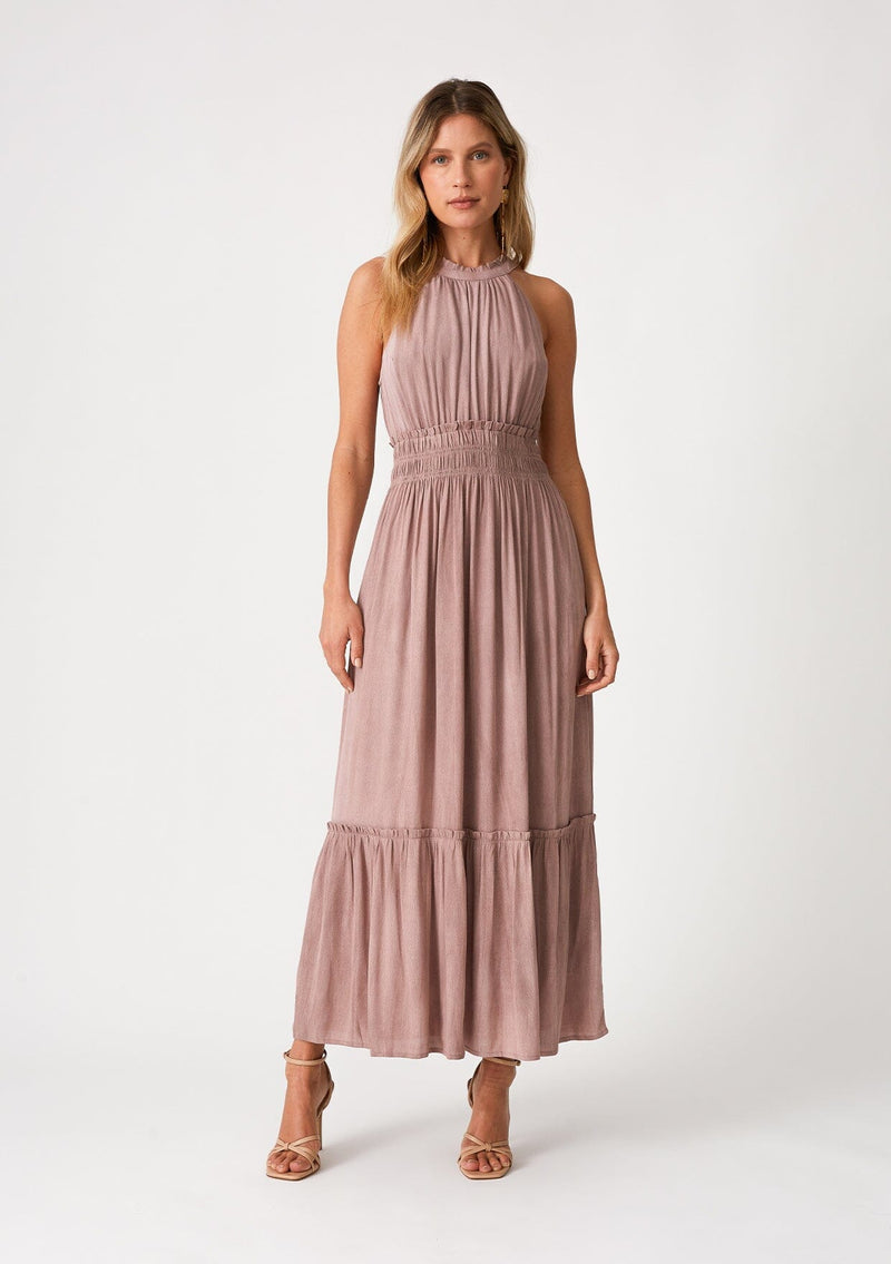[Color: Rose Water] A front facing image of a blonde model wearing a pink bohemian maxi dress in a soft pink vintage wash. With a ruffle trimmed halter neckline, a smocked elastic waist, a tiered long skirt, and a back keyhole detail with an adjustable tie. 