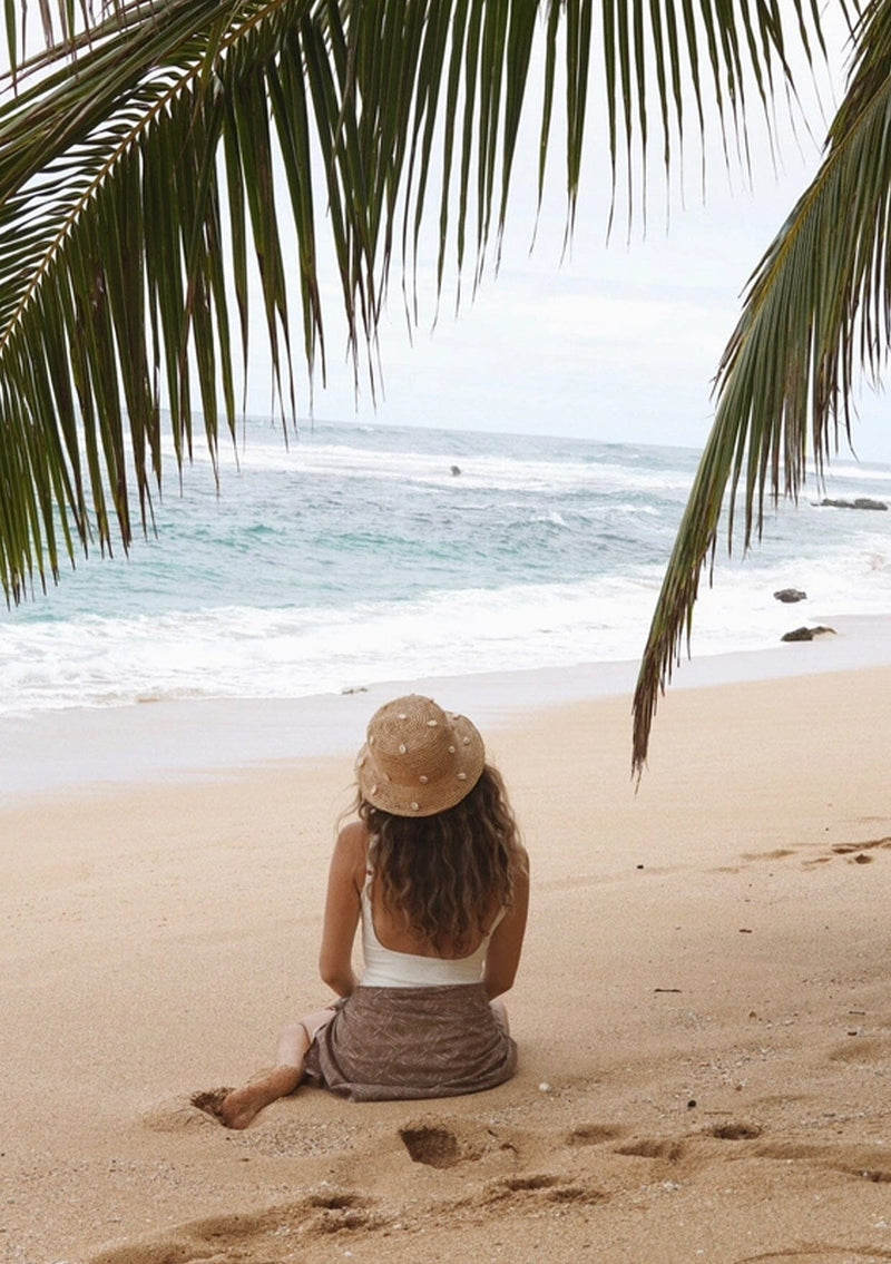 A blonde model wearing a raffia bucket hat with sewn in cowry shells.