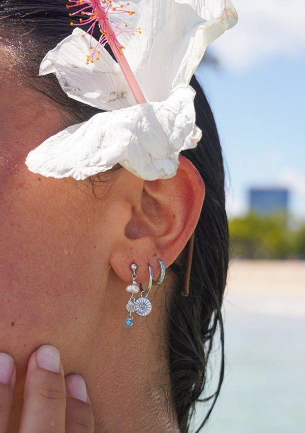 Close-up of an ear with silver earrings, hair adorned with a white flower.