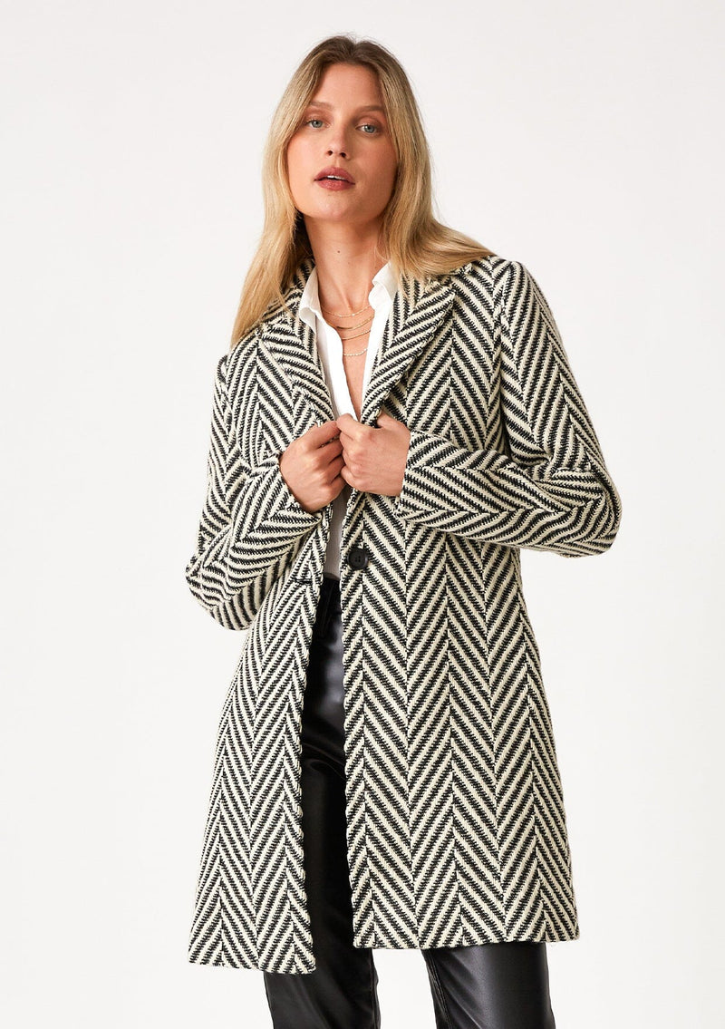 [Color: Cream/Black] A front facing image of a blonde model wearing a classic womens coat in a cream and black chevron stripe. With long sleeves, a notched collar, a button front, and side pockets. 