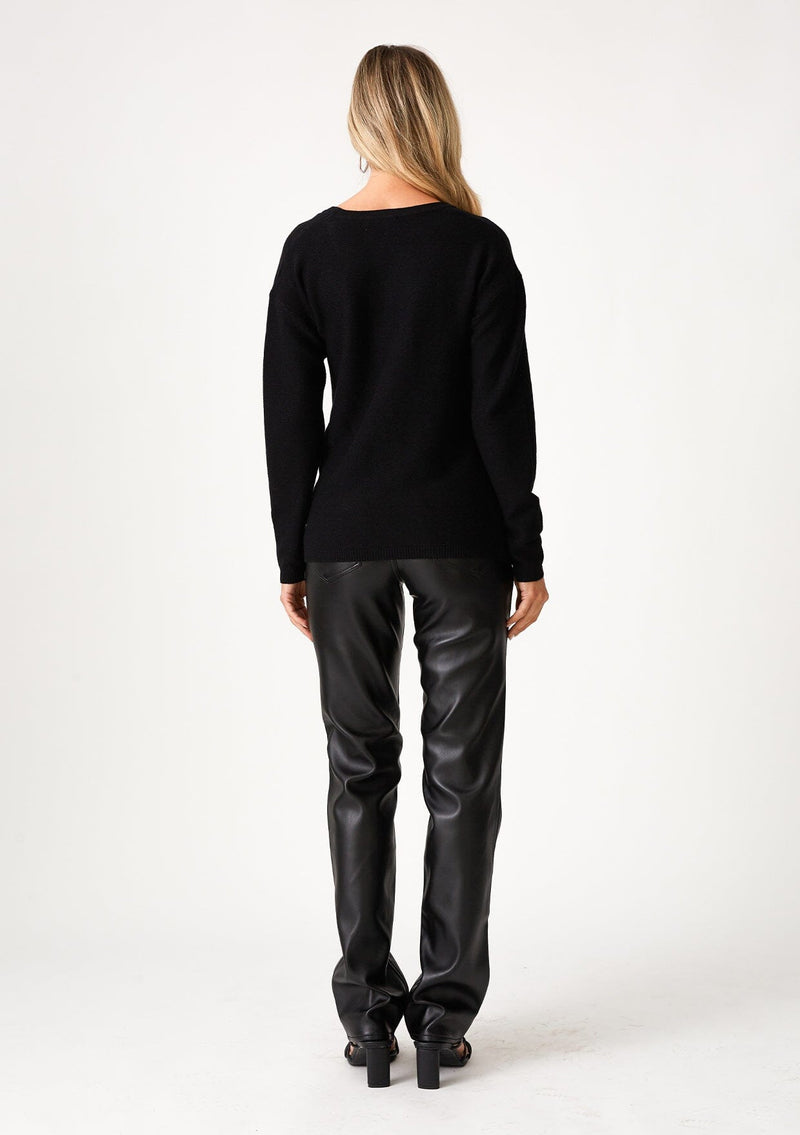 [Color: Black] A back facing image of a blonde model wearing a black pullover sweater in a ribbed textured knit. With long sleeves, a crew neckline, long sleeves, a relaxed fit, and a knot front waist detail.