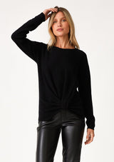 [Color: Black] A front facing image of a blonde model wearing a black pullover sweater in a ribbed textured knit. With long sleeves, a crew neckline, long sleeves, a relaxed fit, and a knot front waist detail.