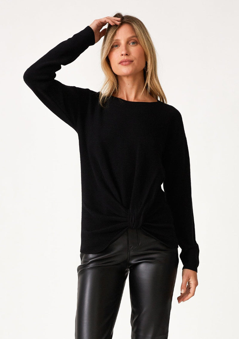 [Color: Black] A front facing image of a blonde model wearing a black pullover sweater in a ribbed textured knit. With long sleeves, a crew neckline, long sleeves, a relaxed fit, and a knot front waist detail.