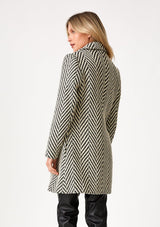 [Color: Cream/Black] A back facing image of a blonde model wearing a classic womens coat in a cream and black chevron stripe. With long sleeves, a notched collar, a button front, and side pockets. 