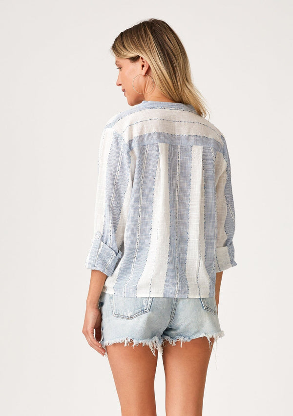 [Color: White/Blue] A back facing image of a blonde model wearing a lightweight white and blue striped top. With long rolled sleeves, a tie front detail, and a concealed button up front.