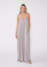 [Color: Lilac Dove] A front facing image of a blonde model wearing a light purple sleeveless maxi dress with gold metallic thread details. With adjustable spaghetti straps, a deep v neckline in the front and back, side pockets, and a loose, oversized flowy fit.