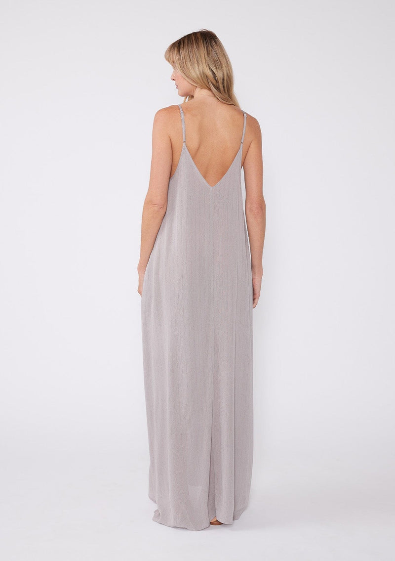 [Color: Lilac Dove] A back facing image of a blonde model wearing a light purple sleeveless maxi dress with gold metallic thread details. With adjustable spaghetti straps, a deep v neckline in the front and back, side pockets, and a loose, oversized flowy fit.
