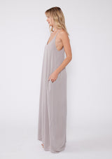 [Color: Lilac Dove] A side facing image of a blonde model wearing a light purple sleeveless maxi dress with gold metallic thread details. With adjustable spaghetti straps, a deep v neckline in the front and back, side pockets, and a loose, oversized flowy fit.