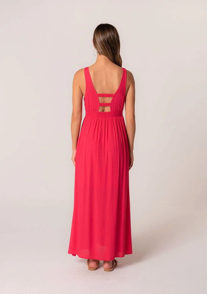 [Color: Hot Pink] A front facing image of a brunette model wearing a bohemian sleeveless spring maxi dress in hot pink. With a self covered button front, a deep v neckline, a front slit, a smocked elastic empire waist, and an open back with elastic strap detail.