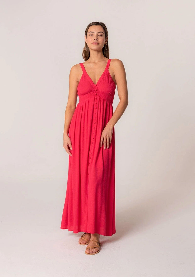 [Color: Hot Pink] A front facing image of a brunette model wearing a bohemian sleeveless spring maxi dress in hot pink. With a self covered button front, a deep v neckline, a front slit, a smocked elastic empire waist, and an open back with elastic strap detail.