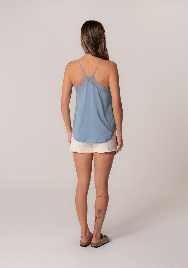 [Color: Denim] A back facing image of a brunette model wearing a blue camisole tank top. With spaghetti straps, a v neckline, lace trim, a racerback, and a relaxed fit. 