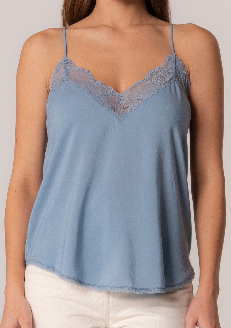 [Color: Denim] A close up front facing image of a brunette model wearing a blue camisole tank top. With spaghetti straps, a v neckline, lace trim, a racerback, and a relaxed fit. 