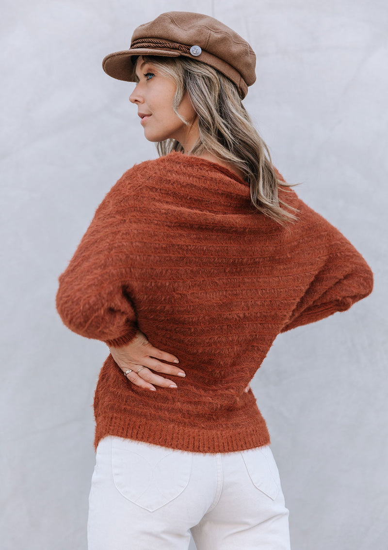 [Color: Burnt Orange] A blonde model wearing a fuzzy dark orange boatneck sweater. The wide neckline can be worn off the shoulder.  