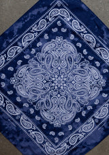 [Color: Navy] A woman wearing a square bandana with a classic paisley print throughout in a trendy tie dye wash. 