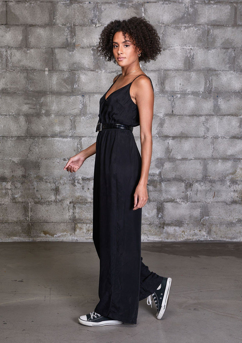 [Color: Black] A woman wearing a one piece jumpsuit. Featuring a wide leg, a front keyhole detail, an elastic cinched waist, and side pockets.