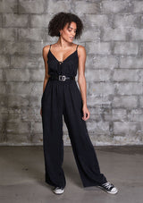 [Color: Black] A woman wearing a one piece jumpsuit. Featuring a wide leg, a front keyhole detail, an elastic cinched waist, and side pockets.