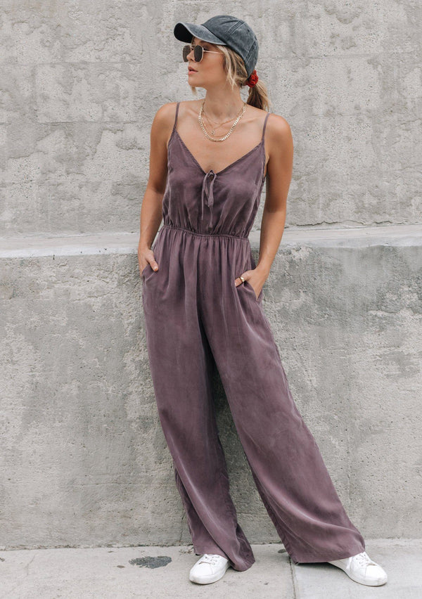 [Color: Charcoal] A woman wearing a one piece jumpsuit. Featuring a wide leg, a front keyhole detail, an elastic cinched waist, and side pockets.
