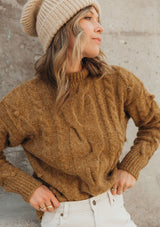 [Color: Tobacco] A gorgeous cable knit pullover featuring whimsical pom pom details, a warm mock neck, and a contrast ribbed trim.